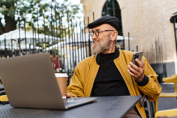 A fashionable senior man relaxes at an outdoor cafe, surrounded by urban charm.