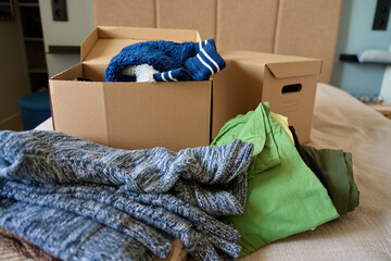 Open donation box filled with donated clothes on bed. Cardboard box with used clothes for recycling...