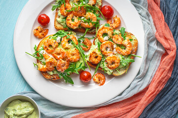 Toast with shrimp, avacado and arugula with tomatoes on a white plate on a blue background with a napkin. The concept of a healthy breakfast. Close-up.