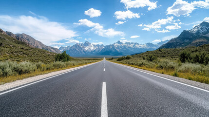 Naklejka premium scenic view of long, open road stretching towards majestic mountains bright blue sky