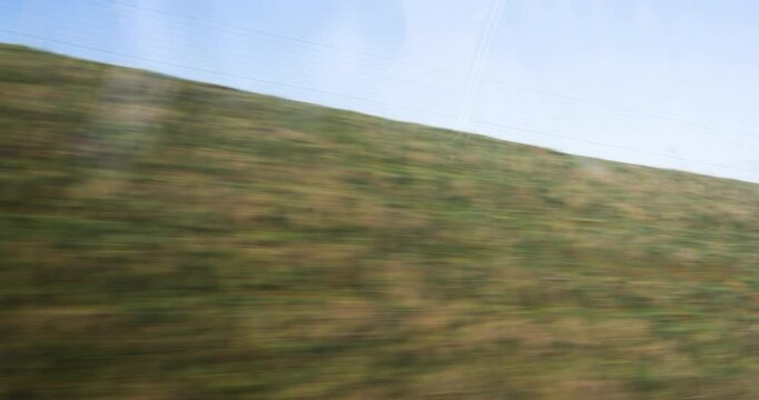 A serene view from a high-speed train in France showcases vibrant green fields and distant hills, blending peaceful rural settings with swift modern travel 4k DCI
