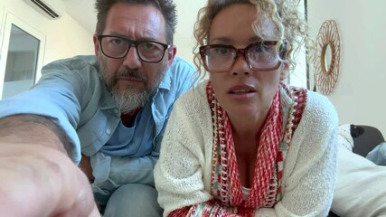 Confused middle-aged couple sitting on couch at home, struggling to access online account, dealing with login error, security warning, suspicious activity, or possible cyber scam