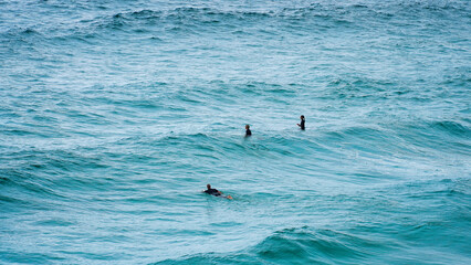 Surfers ride the waves in a vibrant ocean under a cloudy sky at midday