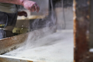 Baker dusting flour over work surface in traditional bakery
