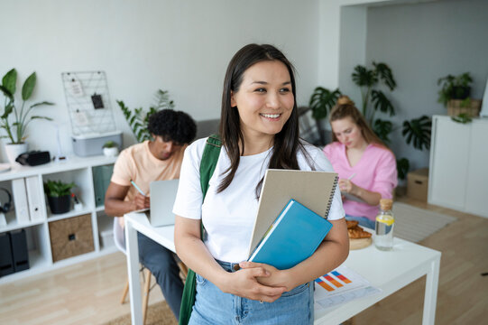 Young woman smiling while holding notebooks in a collaborative study environment with peers