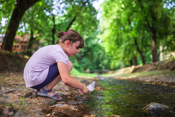 Young girl launching paper boat into stream in lush park