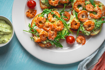 Toast or sandwiches with avocado oil, arugula and fried prawns on a white plate on a light blue background with a napkin. Healthy breakfast. View from above. Flat layout. Space for text.
