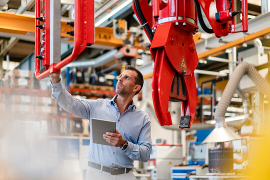 Male entrepreneur analyzing claw machine while holding digital tablet in industry
