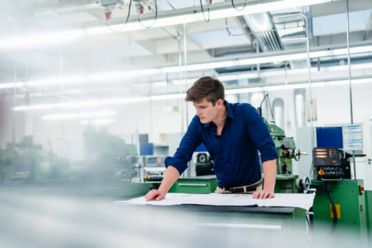 Male professional examining blueprint while working on desk in industry