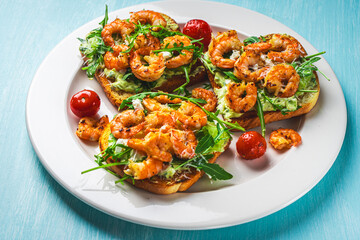 Toast with shrimp, arugula and avocado on a white plate with cherry tomatoes on a blue table. Space for text. Healthy and tasty breakfast concept. Top view. Flat lay.