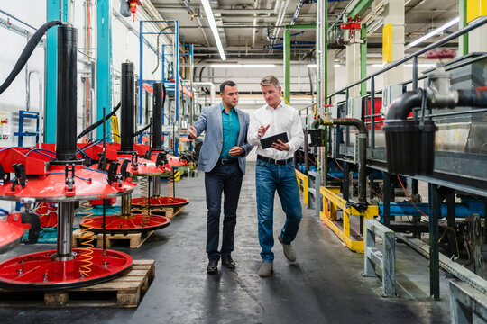 Mature businessman with male colleague discussing over digital tablet while walking in industry