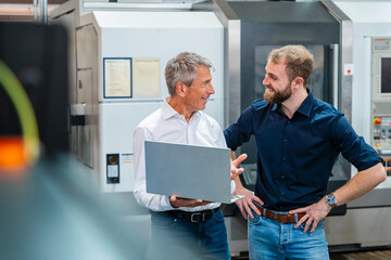 Two men discussing in a production hall with a laptop