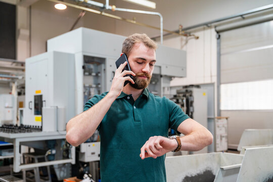 Man in a production hall talking on the phone and checking his watch