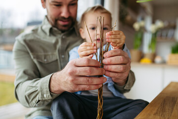 Father and little boy braiding easter whip from willow branches. Easter tradition concept. © Halfpoint