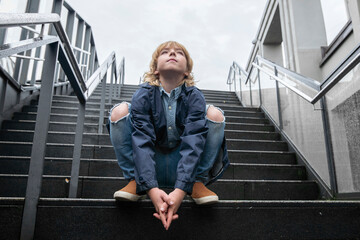 Portrait of blond boy crouching on stairs outdoors looking up