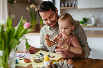 Little boy and father painting eggs with brush and easter egg dye.
