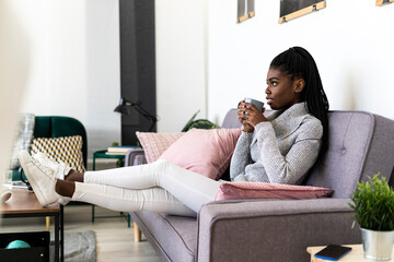 Thoughtful young woman drinking coffee while sitting on sofa in living room at home