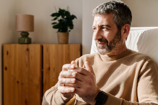 Man sitting indoors with hands clasped, wearing a sweater and watch