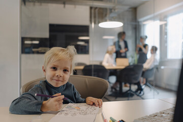 Portrait of smiling boy painting in office with business team having a meeting