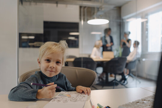Portrait of smiling boy painting in office with business team having a meeting
