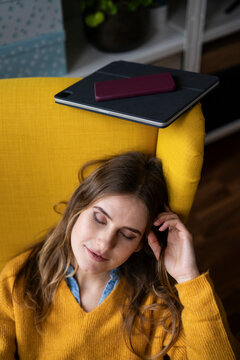 Woman relaxing in a yellow armchair with a tablet and smartphone at home