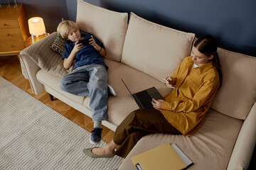 Mother and son using digital gadgets on a sofa at home