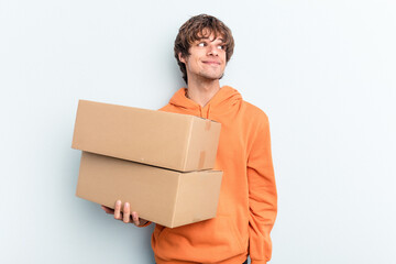 Young man making a move while picking up a box full of things isolated on blue background dreaming...