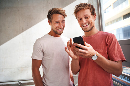 Two happy young men sharing smartphone