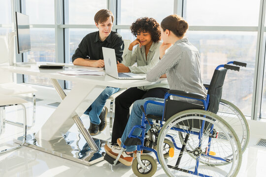 Teamwork brainstorm. Diverse multiracial colleagues woman in chair for people with disability working together. Group of people sitting in creative office discussing business. Young professional team