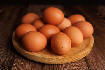 Wooden plate full of brown eggs on dark wooden table, symbolizing the rising prices of eggs in the market