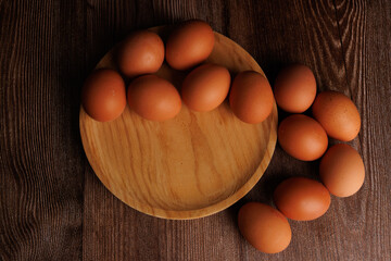 Fresh brown eggs in wooden plate on dark background, representing the financial strain of grocery price hikes