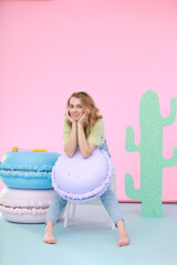 A young woman in a light casual outfit sits on a white step stool in a vibrant photo zone. She...