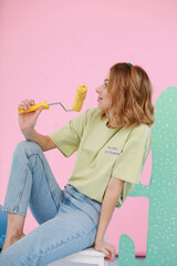 A young woman in a light casual outfit sits on a white step stool in a vibrant photo zone. She...