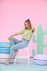 A young woman in a light casual outfit sits on a white step stool in a vibrant photo zone. She...