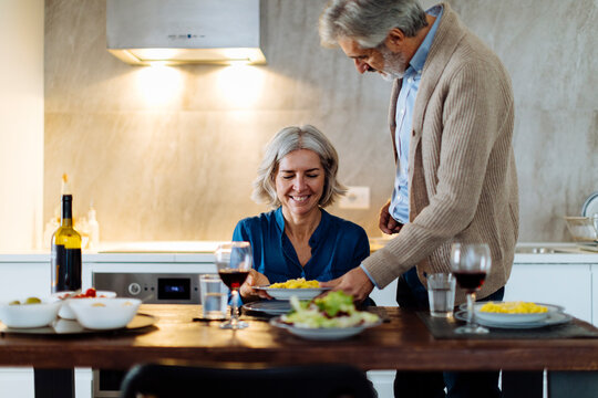Mature man serving dinner to his wife in kitchen at home