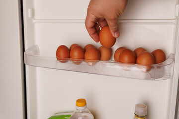 Close-up of a hand taking an egg from a fridge shelf reflecting inflation and rising grocery expenses