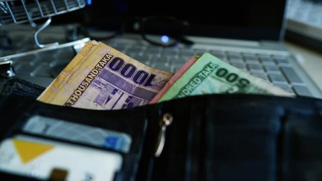 Wallet with Bangladeshi Taka on Laptop Keyboard, A wallet containing Bangladeshi Taka notes and credit cards is placed on a laptop keyboard