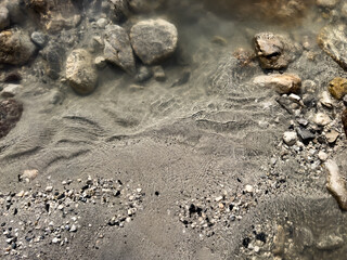 soft ripples on a pebble river bank with large rock formations underwater. natural abstract texture with a calm, earthy aesthetic