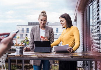 Two women collaborating on a project with a tablet in an outdoor office setting