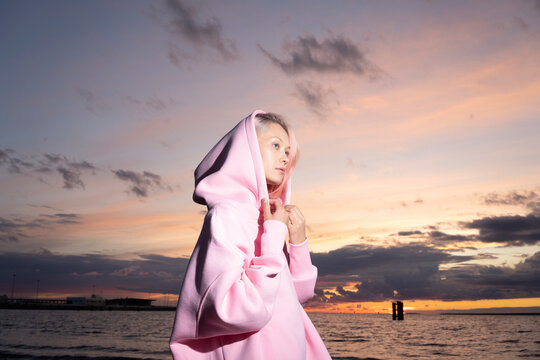 Young woman wearing pink hooded shirt standing on beach at sunset