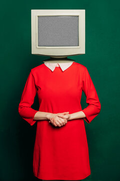 Stylish woman in a vintage red dress with a monitor on her head against a green background