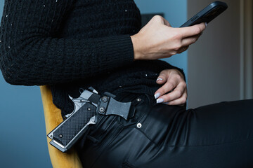 The girl has a gun in her holster, the girl is sitting on a chair and holding a mobile phone in her...
