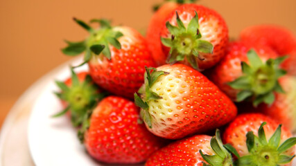 Close-up of ripe and slightly unripe strawberries piled on a white plate and juicy texture. 