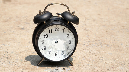 Close-up of a black alarm clock lying on a rough concrete surface with its glass face shattered broken timepiece symbolizes lost time, Concept of time running out.