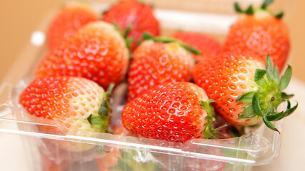 Close-up of ripe, juicy strawberries with green stems in a clear plastic container vibrant red...