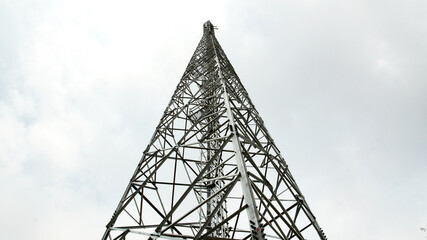 Low-angle view of a tall steel telecommunications tower emphasizing its intricate metal framework and towering height, structure stands against a cloudy sky symbolizing connectivity and modern infrast