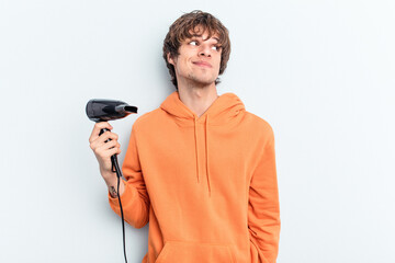 Young caucasian man holding a hairdryer isolated on blue background dreaming of achieving goals and...