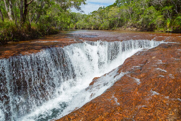 Eliot creek waterfall falls into a fissure in the rock that forms its bed, and down into a deep, pristine creek that flows into a popular but remote swimming hole on Cape York in tropical Australia.