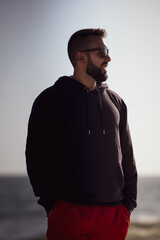 Young man with beard and glasses on the beach in Santa Monica, California in sweatshirt