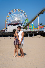 Loving couple sightseeing on the Santa Monica pier by the beach, looking at each other and holding hands.